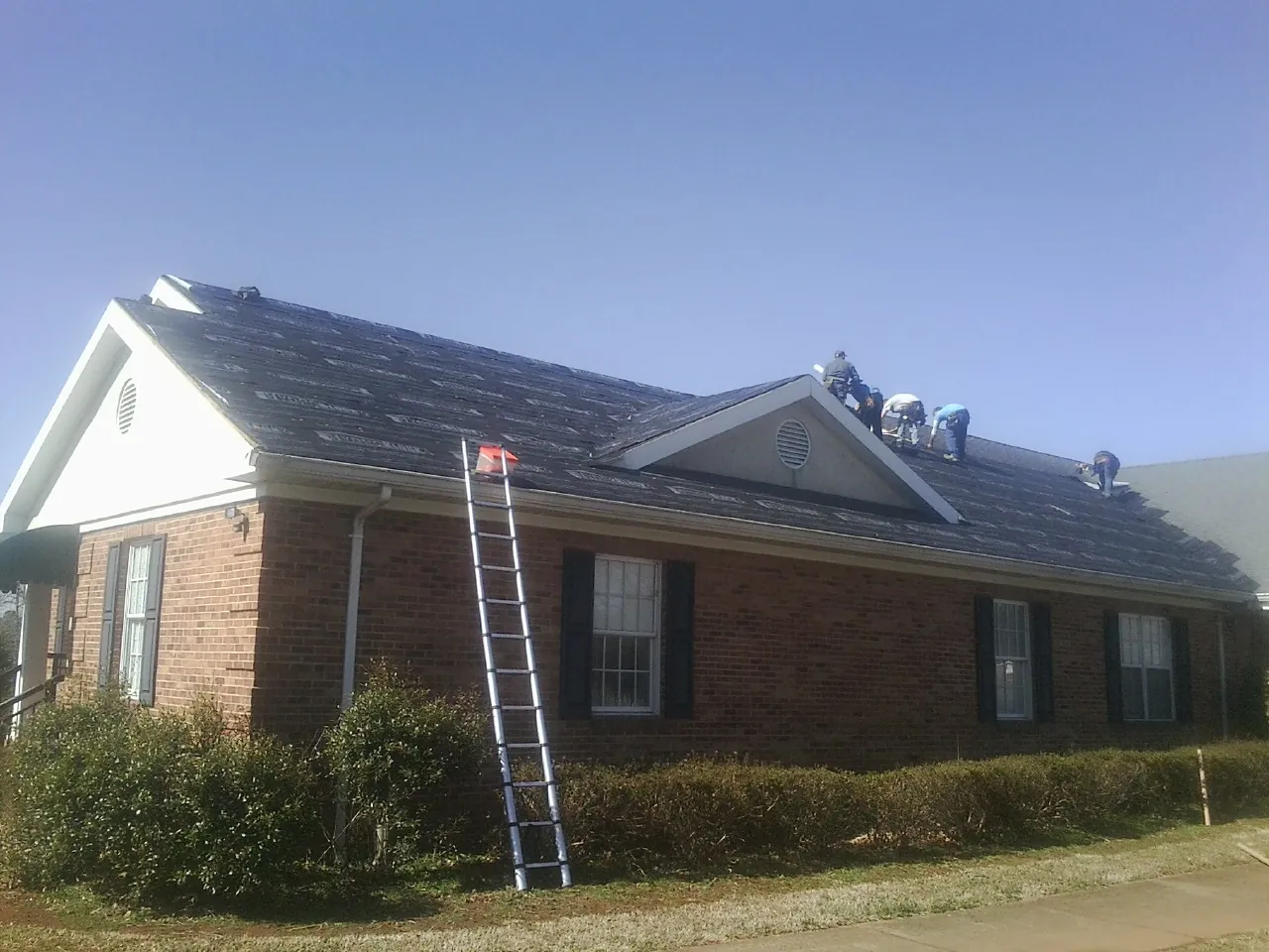 Crew tearing shingles off a brick ranch roof with a ladder set — Metal Roof Repair work by our crew in Camden